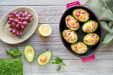 Top view on grilled avocado boats with bacon and quail eggs, flat lay on wood