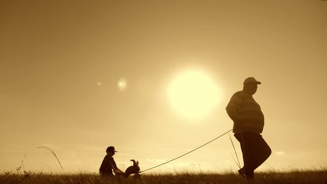 Senior man grandfather teaches his grandson to ride a bike in nature. He pulls it by the rope, the kid learns to ride a bicycle, fun for the family in the outdoor during sunset. Generation concept.