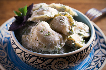 Dumplings filled with potato in sour cream, blue bowl on wooden table