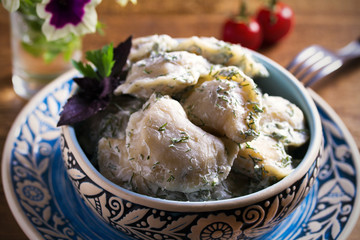 Dumplings filled with potato in sour cream, blue bowl on wooden table