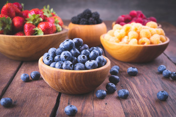 Blueberries in a wooden bowl and other berries on a dark wooden old background in vintage style.