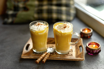 Two glass cups of pumpkin spice latte next to a window