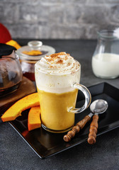 A glass of spicy pumpkin cappuccino on grey background
