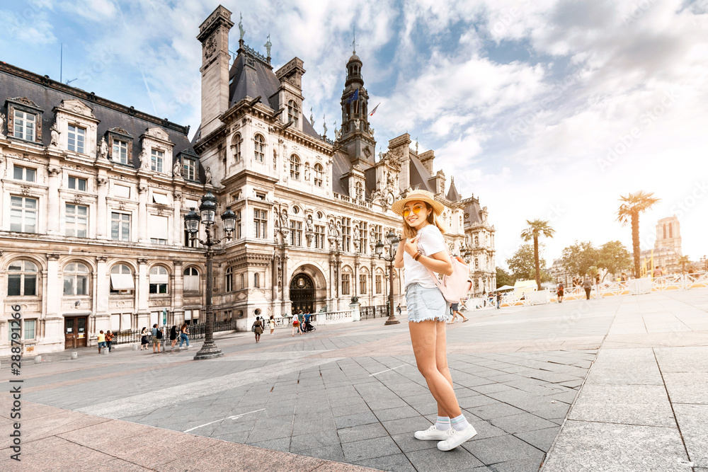 Wall mural Attractive girl traveler with a cute backpack enjoys the view of the stunning Gothic architecture of the old town Hall in Paris. Your holidays and adventures in Paris - Wall murals