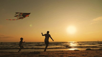 Happy family father and child daughter launch a kite on beach at sunset. Funny family time. Concept of friendly family, travel and freedom.
