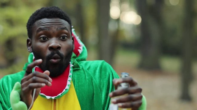 Portrait of surprised young expressive man in dino costume looking at somebody with excitement emotional prankster staying in the park outdoors.