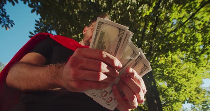 Low angle view of young man calculating bundle of money banknoytes feeling unsatisfied with salary standing outdoor in the park.