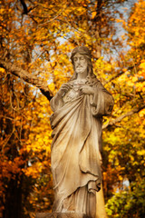 Obraz premium Anient statue if Jesus Christ against a background of golden autumn leaves in the sun's rays