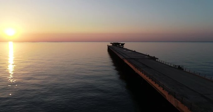 vuelo dron sobre final puente pantalan de puerto abandonado en un amanecer anaranjado y el sol despuntando