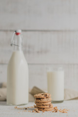 Galletas en primer plano con botella de leche detrás y fondo blanco de madera