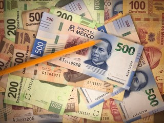 Mexican pesos bills spread randomly over a flat surface with a pencil on top