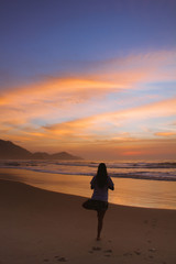 Fototapeta premium Woman doing yoga at sunrise in the beach of Ubatuba, Sao Paulo, Brazil