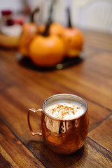 Golden color's mug of coffee on wooden table of a restaraunt during the Halloween holiday in new York. Table decorated by pumpkins.