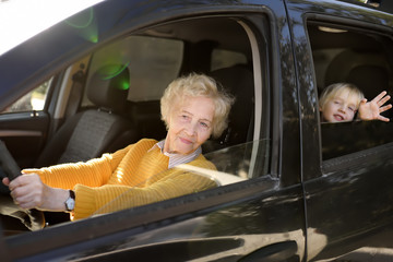 An elderly woman, grandmother or nanny, is driving a child in a car to kindergarten.