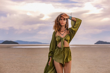 beautiful young woman in stylish costume on the beach at sunset
