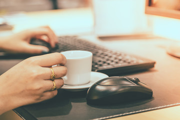 Woman hand holdding coffee cup with working table