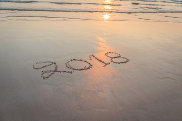 Numbers 2018 handwritten on sand at the beach during sunset time
