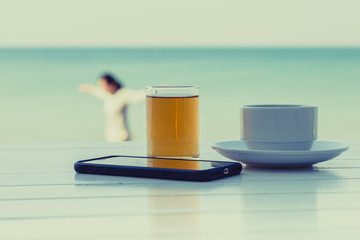Tea coffee with smart phone on the white wooden table at the beach