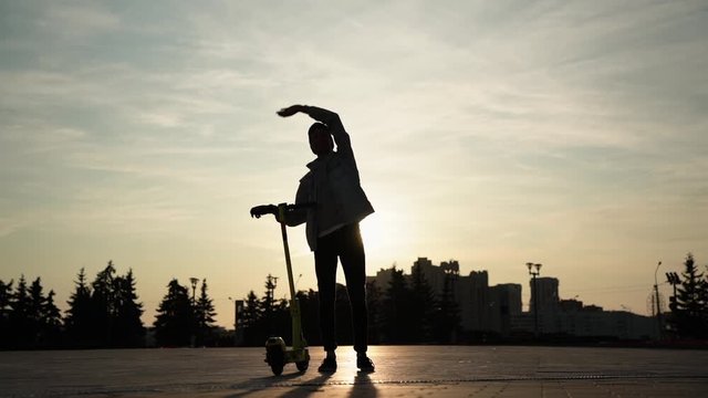 Silhouette of man with scooter, who waving hand high and shows thumbs up, slowmo