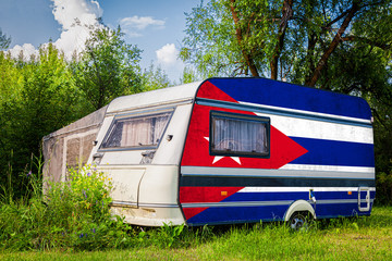A car trailer, a motor home, painted in the national flag of  Cuba stands parked in a mountainous. The concept of road transport, trade, export and import between countries.