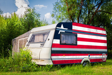 A car trailer, a motor home, painted in the national flag of  Liberia stands parked in a mountainous. The concept of road transport, trade, export and import between countries.