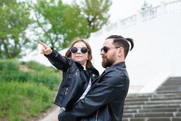 Fashionable stylish family for a walk. Daughter in the hands of dad. Point fingers. Time together....