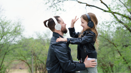 Charming little girl and her handsome young dad in headphones are listening to music. Photo v-sign...