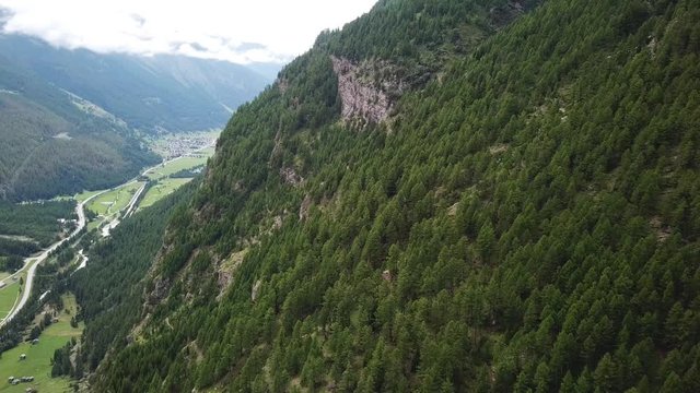 scenic flight along a valley with green pine forest. drone flight along fir forest mountain on a cloudy day in randa wallis switzerland.