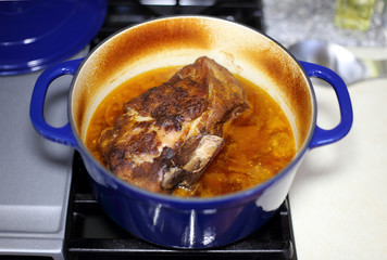 Braised pork roast cooked in a Dutch oven resting on the stove top.