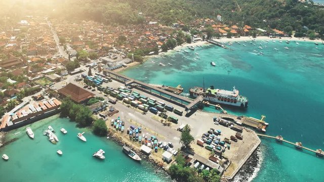 wonderful Nusa Penida harbour with town buildings on coast surrounded by forests and pier on sunny day aerial view. Concept travel transport tourism. Tropical Bali island, Indonesia. Cinematic 4K