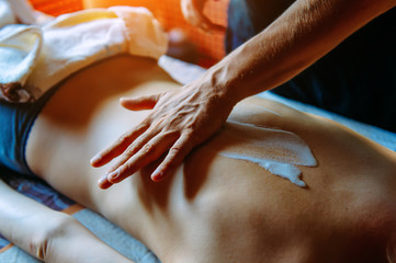 Applying moisturizing cream on the female back before massage - close-up. People, beauty, healthy lifestyle and relaxation concept -  woman lying and having back massage with cream at spa.