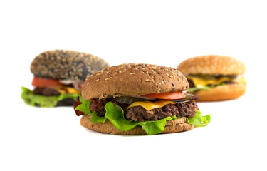 Big burger close up on a white background. Beef patty burger, cheddar cheese, lettuce, bacon, pickled cucumber, tomato and balsamic sauce. In the background are two burgers.