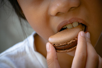 Kid eating Chocolate Macaron or Chocolate Macaroon. It's a colorful small and sweet French pastry of made of almond flour and egg whites.