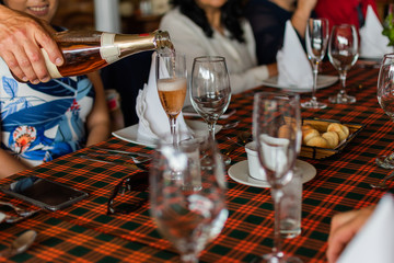 champagne bottle served in full glasses next to empty glass in celebration of marriage with couple and family behind on restaurant