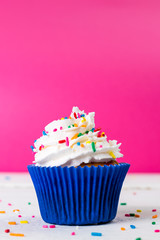 Cupcake saboroso de baunilha com chantily e brigadeiro granulado colorido sobre chuva de esferas azuis mais vela chuva de prata