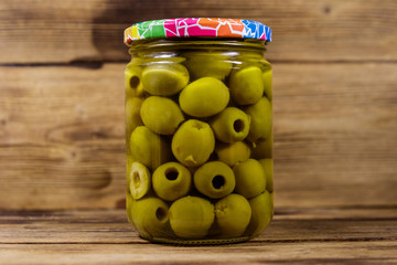 Pickled green olives in glass jar on wooden table