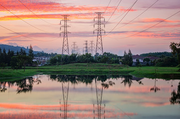 View before sunset with beautiful clouds and sun before the horizon. There are high voltage electricity poles and cables. Reflection from the lake water