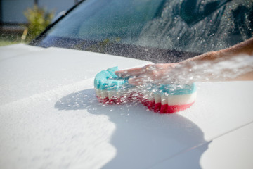 man washing a soapy white car with a colorful sponge.Manual car wash in car wash shop service with...