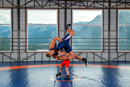 A  wrestler boy in a sports tights wrestles with an adult male wrestler on a wrestling carpet in the gym. The concept of child power and martial arts training. Teaching children Greco-Roman wrestling