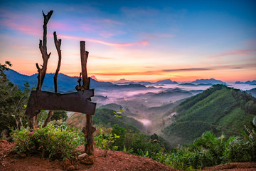 High views with views of mountains and fog interspersed among lush green forests at sunrise, golden light, sky and colorful clouds.