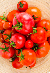 Wooden dish with different ripe tomatoes on white background.