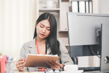 Concentrated young business woman working in office, charming Asian woman accountant looking documents and working on computer