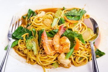 Close up delicious yellow fried noodles with soy sauce, prawns, vegetables and mushrooms on the white plate background. Thai stir-fried noodles (Pad See-Ew). Top view with copy space.