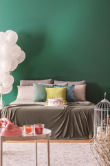 Colorful pillows and birthday cake with candles on king size bed in lovely bedroom, copy space on the empty wall