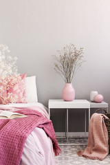 Dry flowers in pastel pink vase on simple nightstand table next to bed