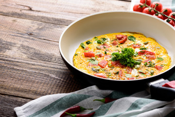 fried eggs in a frying pan close up with cherry tomatoes and greens in a low key on a wooden background with copy space