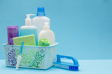 Bottles of dishwashing liquid in basket, sponges and brushes on blue background.