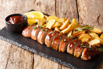 Traditional baked pork tenderloin with potato wedges close-up on a slate board. horizontal