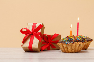 Tasty birthday muffin with burning festive candle and gift boxes.