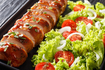 Baked pork tenderloin in honey-garlic sauce with fresh salad close-up on a plate on the table. horizontal